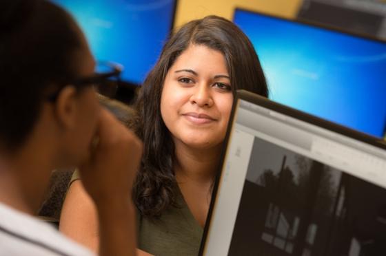 Photo of a Chatham University student in a computer lab talking to a student behind her.